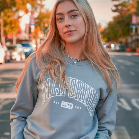Woman wearing a gray sweatshirt with 'California' text on a street background