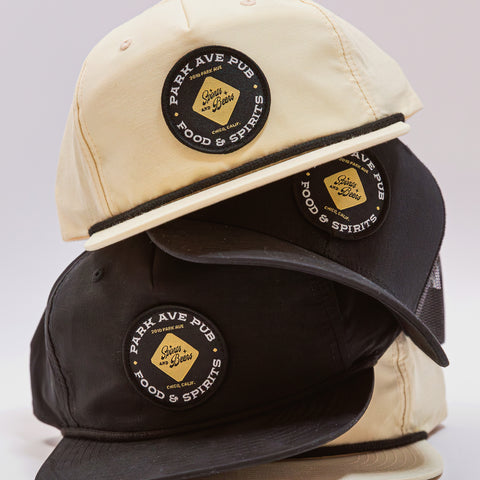 Two baseball caps, one beige and one black, with 'Park Ave Pub' logos on a light gray background.
